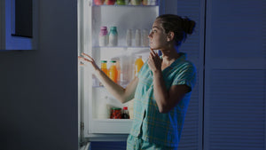 A woman standing in front of an open fridge at night.