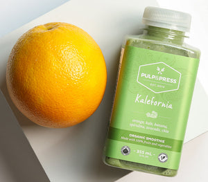 An orange beside a bottle of Kalefornia juice