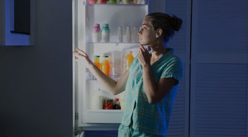 A woman standing in front of an open fridge at night.