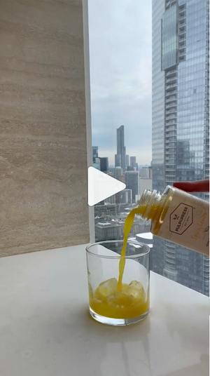 person making a mocktail using cold pressed juice from pulp & press in front of balcony window