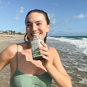 person smiling holding envy pulp & press juice on tropical beach with ocean waves